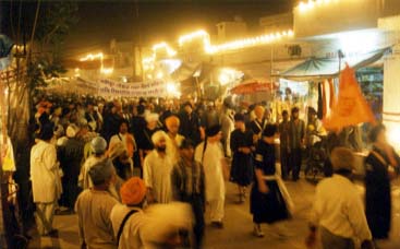 Anandpur street filled with people and lit up with lights.